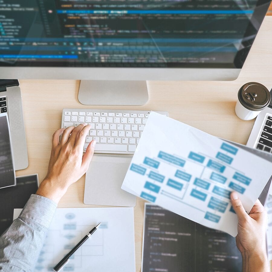 Person using computer and holding a piece of paper with a workflow printed on it